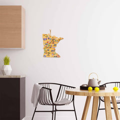 A modern kitchen showcases sleek black chairs and a wooden round table, accented with a teapot and vibrant yellow fruits. Draped over one chair is a gray blanket, while the Minnesota Cutting Board with Artwork by Fish Kiss™ from Totally Bamboo adds charm to the setting. Overhead, a map of Minnesota adorns the white wall, illustrating various regional features.