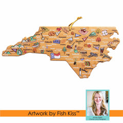 The North Carolina Cutting Board by Totally Bamboo features colorful icons and place names, showcasing cities, foods, and local symbols unique to the state. A small inset of a smiling woman with long hair is included alongside the text "Artwork by Fish Kiss™." This state-shaped cutting board offers a distinctive bamboo surface.