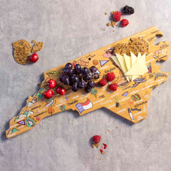 The North Carolina Cutting Board with Artwork by Fish Kiss™, crafted by Totally Bamboo, beautifully displays the colorful city and landmark art of North Carolina. This bamboo cutting surface is stylishly arranged with grapes, cherries, cheese slices, crackers, and berries against a gray textured background.