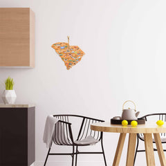 A modern kitchen is enhanced with a black chair, a round wooden table, and a white teapot. A South Carolina cutting board featuring artwork by Fish Kiss™ from Totally Bamboo adorns the white wall. A countertop and geometric vase are partially visible on the left.