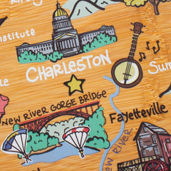 The West Virginia Cutting Board with Artwork by Fish Kiss™, from the brand Totally Bamboo, showcases a stylized map featuring Charleston, highlighted by a prominent building, musical notes, and a banjo. Beneath this lies Fayetteville, displaying the New River Gorge Bridge along with parachutes and a river scene. The illustration rests on a wood texture background that evokes the design of state-shaped cutting boards.