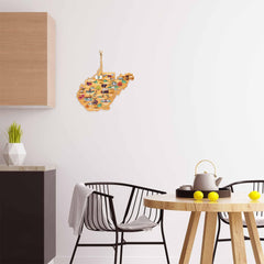 A modern kitchen features a small round table with a teapot and lemons, alongside two black chairs. The West Virginia Cutting Board with Artwork by Fish Kiss™ from Totally Bamboo enhances the white wall displaying a wooden puzzle map with colorful images. A wooden cabinet and a geometric plant vase are also seen.