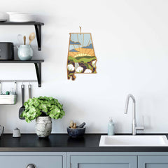 A contemporary kitchen boasts a black countertop, sink, and cabinets. A plant in a white pot adds a touch of greenery next to state-shaped Alabama cutting boards from Totally Bamboo on display. Above, black shelves house kitchen essentials while the wall showcases a vibrant artwork by Summer Stokes shaped like the U.S. state of Alabama with a landscape design.