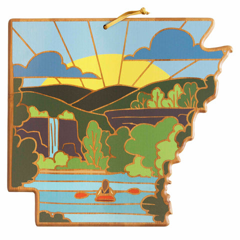 The Arkansas Cutting Board by Totally Bamboo, featuring artwork by Summer Stokes, is shaped like the state of Arkansas and beautifully depicts a kayaker navigating a river and a waterfall surrounded by lush greenery. The vibrant sun shines against a blue sky with clouds, capturing the essence of nature that appeals to any outdoor enthusiast.