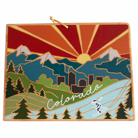 The Colorado Cutting Board with Artwork by Summer Stokes, brought to you by Totally Bamboo, presents a breathtaking illustration of a Colorado mountain landscape. It beautifully features stylized trees, majestic mountains, and a city skyline set against a vibrant sunset backdrop. The essence of adventure is captured with the depiction of a skier in the foreground, elegantly highlighted by "Colorado" inscribed above.