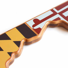 A close-up of a puzzle piece from the Maryland Cutting Board, part of the Totally Bamboo collection featuring artwork by Summer Stokes, showcases a bright and abstract design with vivid colors and shapes. One edge is uniquely wavy, contrasting with the geometric patterns on the surface, similar to state-shaped cutting boards.