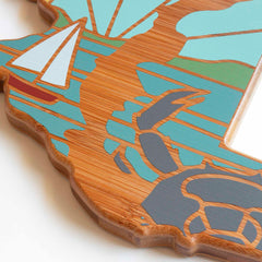 Close-up of the Maryland Cutting Board by Totally Bamboo, showcasing Summer Stokes' wooden artwork. This piece features abstract shapes and colors, including teal, cream, and brown. The design includes geometric patterns and flowing lines with a polished finish and layered texture reminiscent of bamboo cutting surfaces.