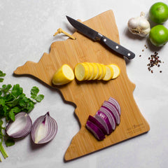 A knife, sliced yellow squash, and red onion rest on the Minnesota Cutting Board with Artwork by Summer Stokes from Totally Bamboo. Fresh cilantro, a halved red onion, garlic bulbs, limes, and peppercorns also adorn the light countertop. This state-shaped cutting board from Totally Bamboo captures the charm of Summer Stokes’ artwork.