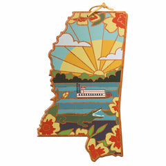 The Mississippi Cutting Board with Artwork by Summer Stokes, from the Totally Bamboo brand, showcases a state-shaped design depicting a river steamboat, sunset, and floral patterns. It artfully includes a swan gliding across the water under a radiant sun with its rays casting over green hills.