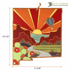 The New Mexico Cutting Board by Totally Bamboo beautifully displays Summer Stokes' artwork, depicting a desert scene that includes cacti, red mountains, a river, and a hot air balloon beneath a radiant sunrise. The bamboo board measures 13-1/2" tall by 11-3/4" wide.