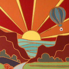 The New Mexico Cutting Board by Totally Bamboo features a vibrant Summer Stokes artwork, depicting a stylized sunset with rays stretching across the sky. The scene showcases mountains and a winding river below, while a hot air balloon drifts in the upper right corner. The color palette consists of warm reds, oranges, and yellows.