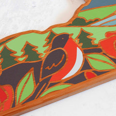 Featuring bold colors and a vibrant nature-themed design, this New York cutting board by Totally Bamboo showcases Summer Stokes' artwork of a robin with an orange-red breast, surrounded by stylized trees and foliage, all enclosed in a wooden frame.