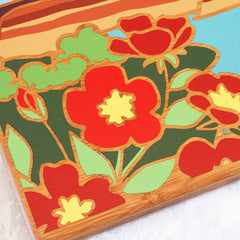 The North Dakota Cutting Board with Artwork by Summer Stokes from Totally Bamboo features a vibrant and stylized design of red and yellow flowers with green leaves, all set against a bamboo surface. Bold outlines are complemented by a light blue sky background, accented with brown and yellow stripes at the top.