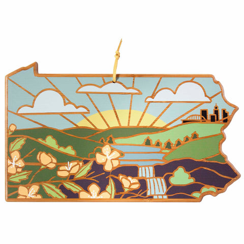 Discover the elegance of Summer Stokes' artwork with the Pennsylvania Cutting Board from Totally Bamboo. Showcasing a stained glass-inspired design, this decorative piece beautifully depicts a sunrise over rolling hills, a peaceful river, and colorful flowers set against a distant city skyline.