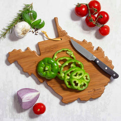 The West Virginia Cutting Board with Artwork by Summer Stokes, from the brand Totally Bamboo, showcases a vibrant arrangement of a sliced green bell pepper, knife, rosemary, garlic, basil, tomatoes, and halved purple onion beautifully placed around it—an enticing tribute to summer cooking.