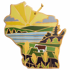 This Wisconsin Cutting Board by Totally Bamboo features Summer Stokes' artwork, depicting the state as a map with a sunset over rolling hills, trees, a cow, and cornfields. The cutting board showcases earthy hues of yellow, green, and brown reminiscent of bamboo surfaces.