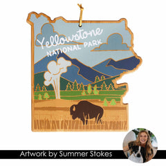 Introducing the Yellowstone Cutting Board with Artwork by Summer Stokes from Totally Bamboo—a beautifully crafted wooden plaque in the shape of Yellowstone National Park, designed to serve as a stunning bamboo cutting surface. The board features stylized UV-printed artwork showcasing vibrant colors of mountains, trees, a bison, and clouds. An inset photo highlights a person smiling with their dog.