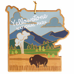 Introducing the Yellowstone Cutting Board with Artwork by Summer Stokes from Totally Bamboo: a wooden masterpiece shaped like the Yellowstone National Park map. This cutting board showcases a stylized bison amid mountains, trees, and a geyser beneath a blue sky, all crafted with precision using UV printing techniques for a vibrant finish on its bamboo surface.