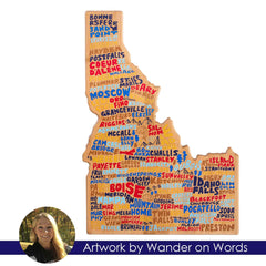 The Idaho Cutting Board with Artwork by Wander on Words™, a product by Totally Bamboo, features a vibrant, state-shaped map adorned with hand-lettered town names. Key cities such as Boise, Coeur d'Alene, and Moscow are prominently highlighted. At the bottom, it includes a photo of the artist and a caption: "Artwork by Wander on Words.