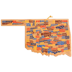 Explore the lively Oklahoma Cutting Board designed by Wander on Words™ from Totally Bamboo. Crafted in the shape of Oklahoma, this board showcases city names like Oklahoma City, Tulsa, and Norman in diverse fonts and colors. It includes a small hole with a string for convenient hanging while you appreciate its charm.