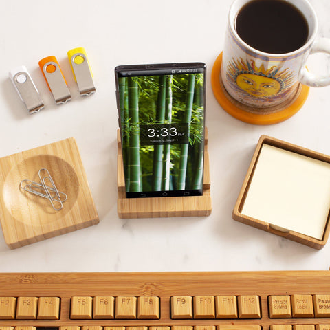 A smartphone showing 3:33 PM is placed on a Totally Bamboo 3-Piece Desk Organizer, accompanied by a sun-themed coffee mug, USB drives, paper clips, sticky notes, and a wooden keyboard on an immaculate white desk.